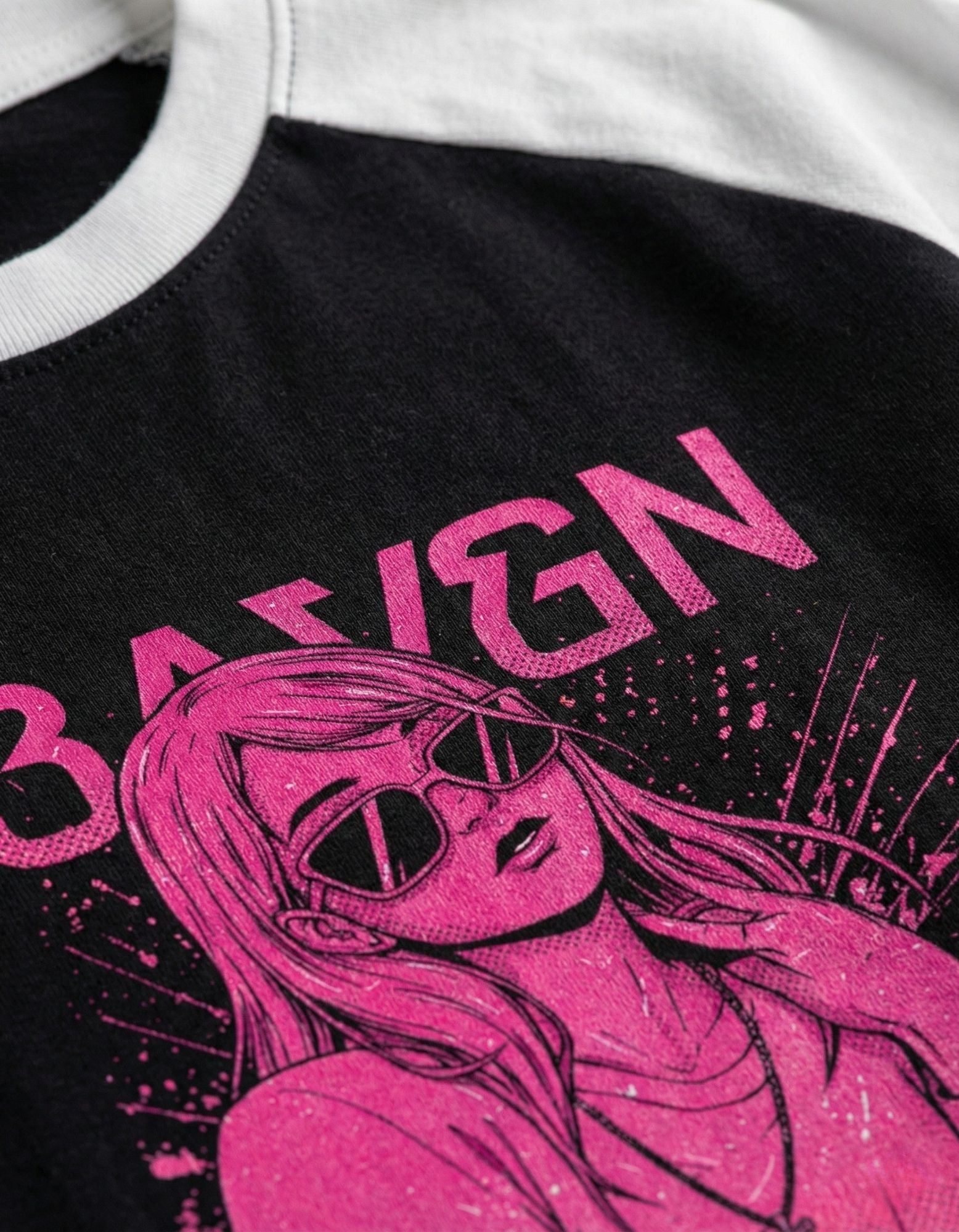 Close-up high-quality detail of the pink "BAYGN" graphic print on a black cotton raglan long-sleeve shirt.