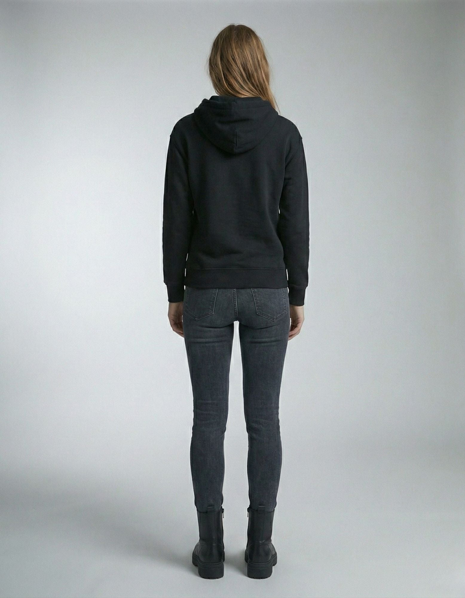 Back view of a female model wearing a premium black oversized hoodie with dark grey denim.
