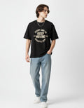 Front view of a black oversized graphic t-shirt for men featuring 'Keep Moving' athletic print, styled with blue jeans.