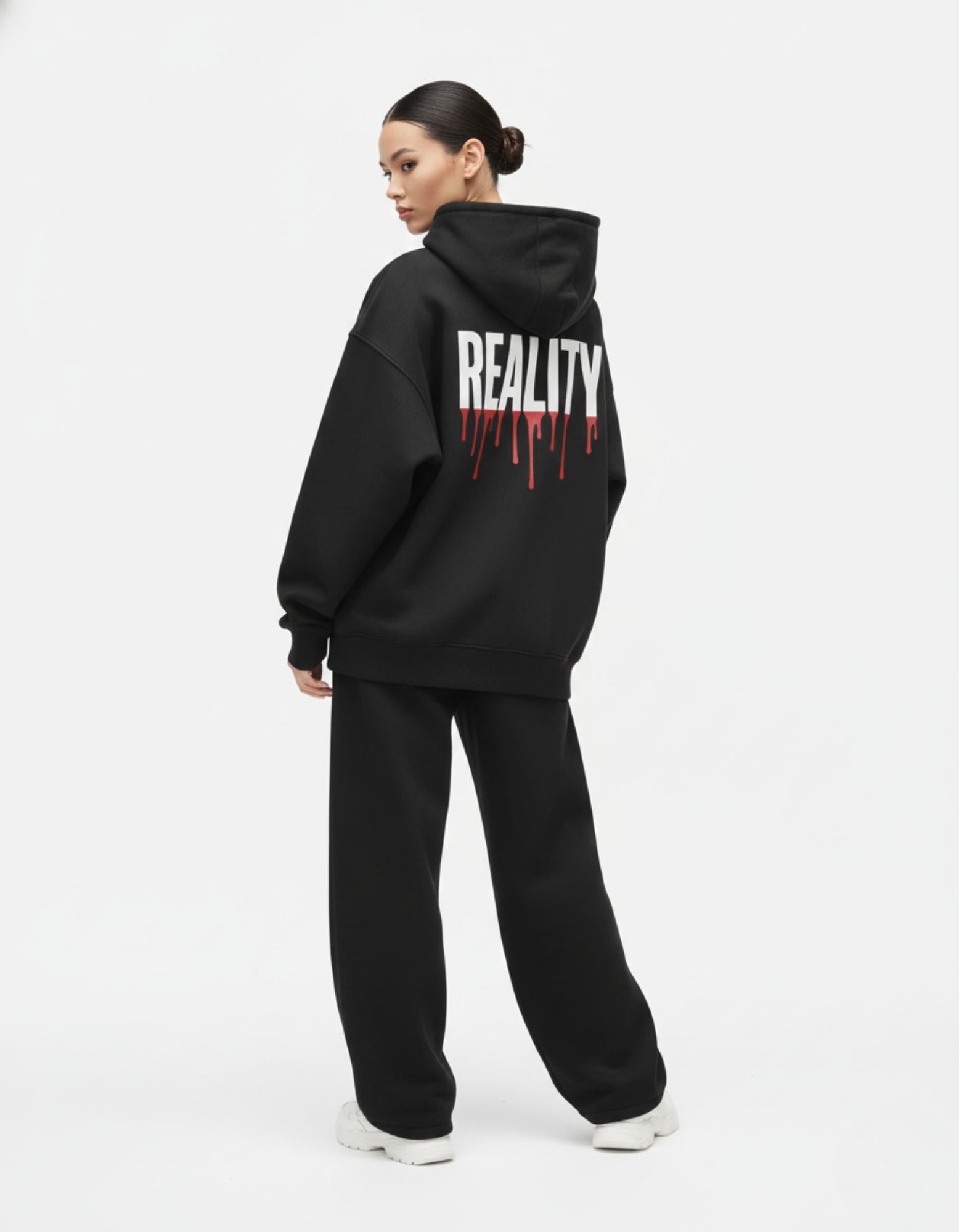"Female model showcasing the back of a GENZs Fashion black oversized hoodie with a bold 'REALITY' drip-style graphic."