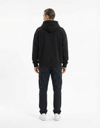 Back view of a male model in an oversized black streetwear hoodie and navy cargo pants, showing the premium relaxed-fit silhouette.