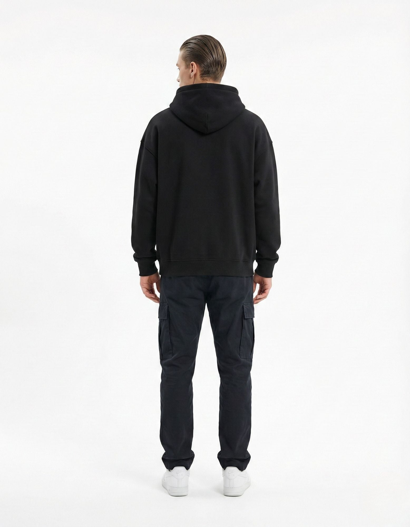 Back view of a male model in an oversized black streetwear hoodie and navy cargo pants, showing the premium relaxed-fit silhouette.