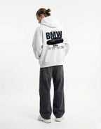 Male model wearing white GENZs Fashion hoodie featuring a detailed BMW M8 back print with car performance statistics.