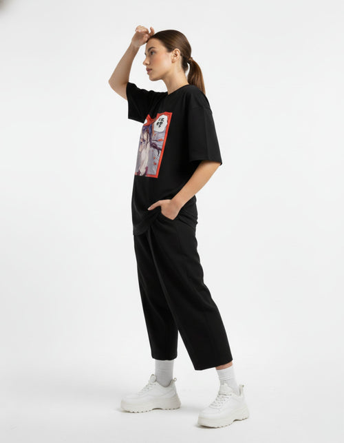 Side view of a female model wearing a black oversized tee with a colorful anime character box graphic and red accents.
