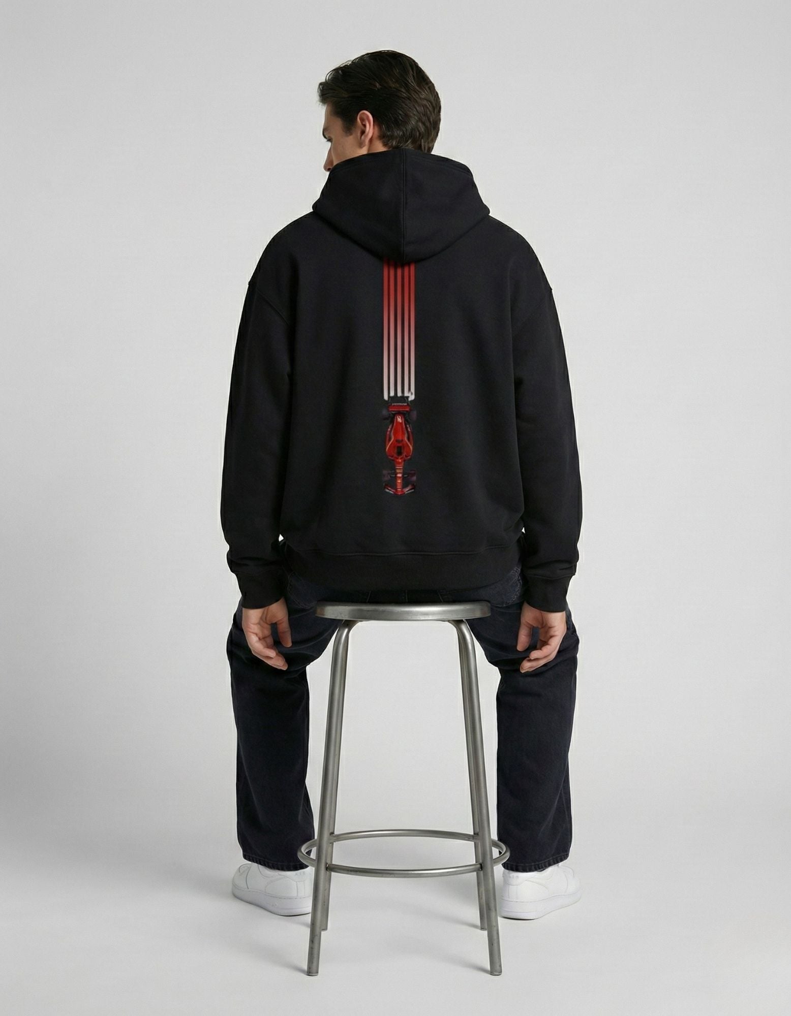 Male model seated showing the detailed F1 racing car back print on a black heavyweight hoodie by GENZs Fashion.