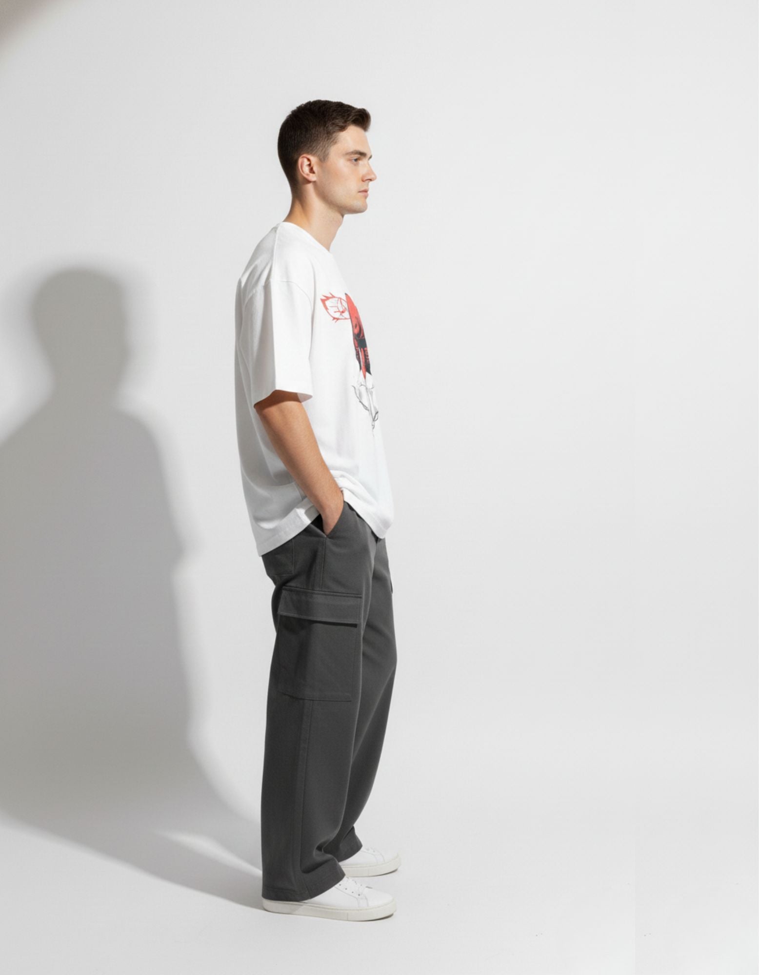 Side profile of male model wearing GENZs Fashion white anime graphic oversized t-shirt and grey baggy cargo pants.