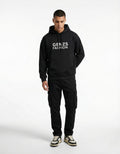 A man wearing a black GENZs Fashion hoodie with white text logo and black cargo pants, a complete urban streetwear look.