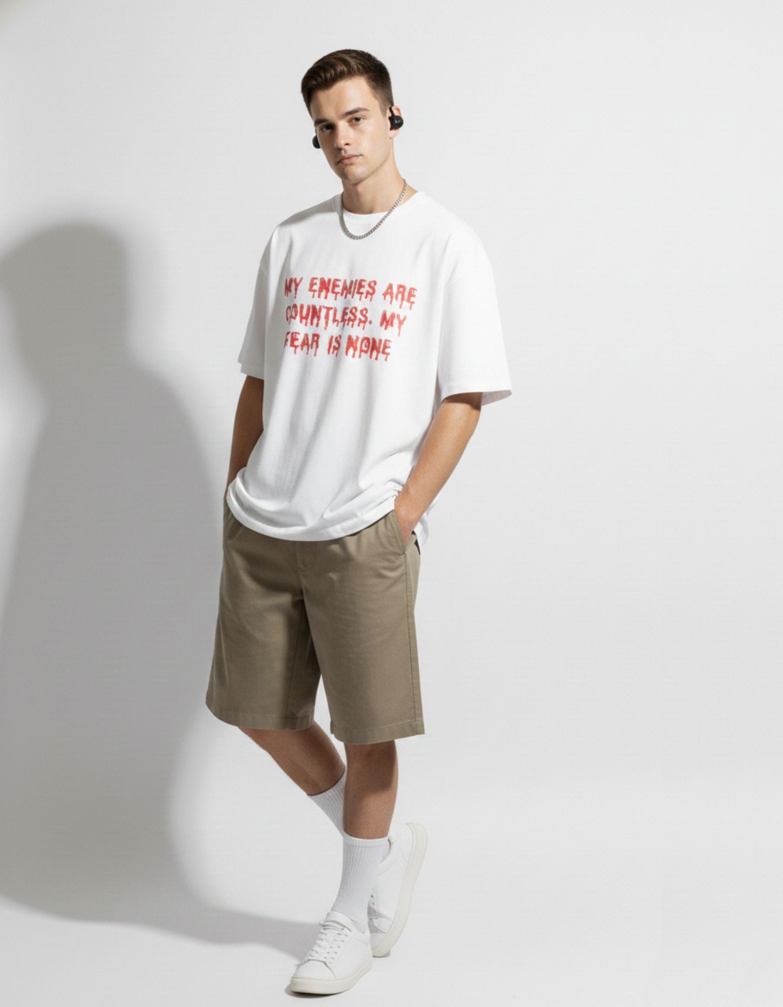 Male model wearing GENZs Fashion white quote oversized t-shirt with beige baggy shorts, premium Indian streetwear look.