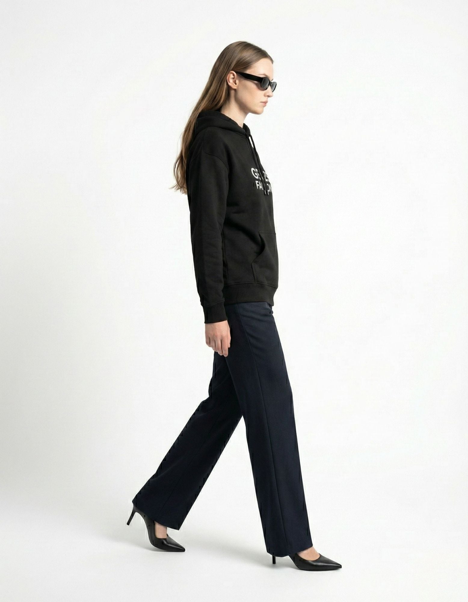 A female model in profile walking wearing a black GENZs Fashion hoodie and sunglasses, representing the modern streetwear brand.