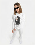 Female model standing in a white graphic sweatshirt with a 'Silent Vision' manga illustration and black sunglasses.