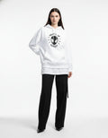 Female model wearing a white "What's Up Danger" Spider-Man graphic hoodie with black trousers and heels for a chic streetwear look.