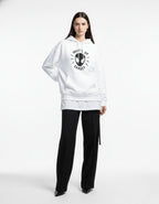Female model wearing a white "What's Up Danger" Spider-Man graphic hoodie with black trousers and heels for a chic streetwear look.