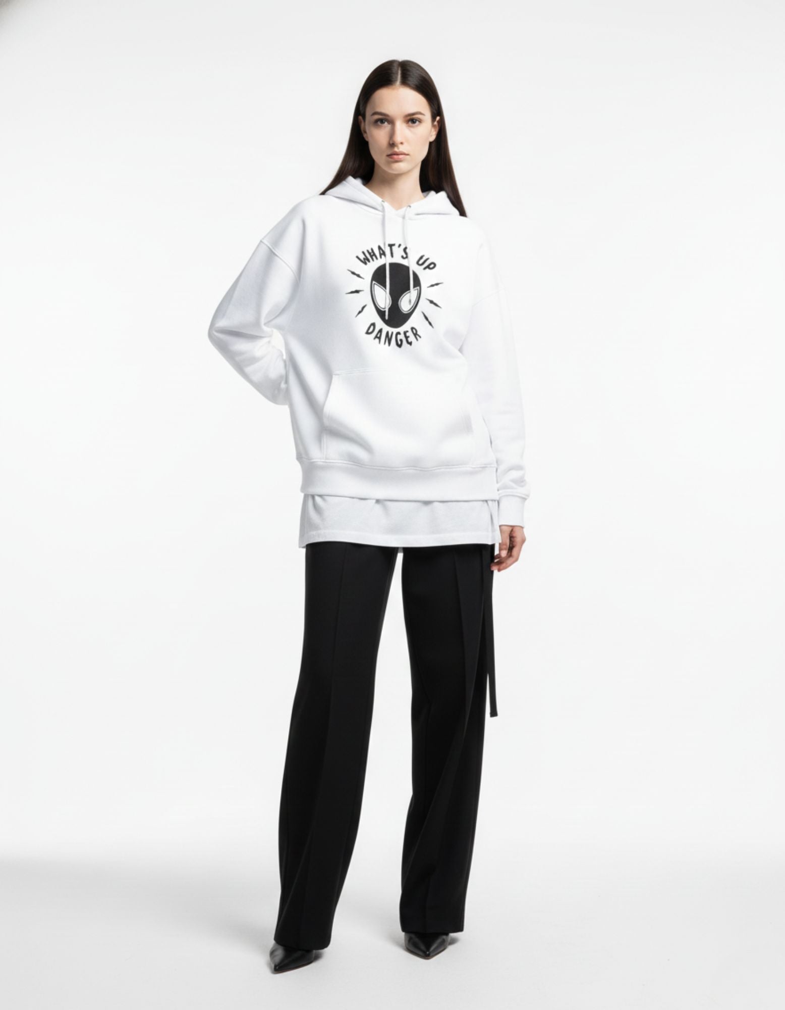 Female model wearing a white "What's Up Danger" Spider-Man graphic hoodie with black trousers and heels for a chic streetwear look.