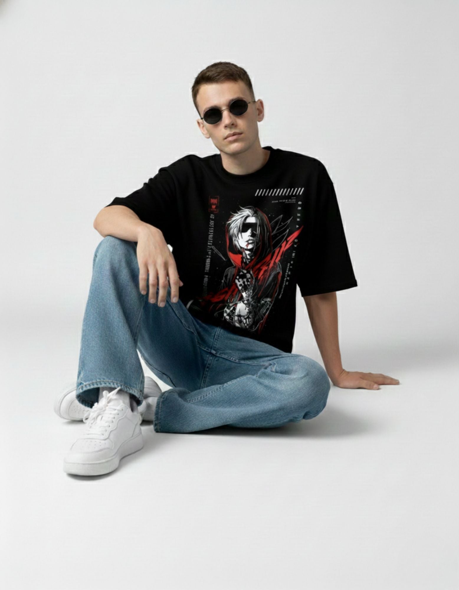 Lifestyle shot of a male model sitting in a black anime-inspired graphic tee and light wash denim jeans.
