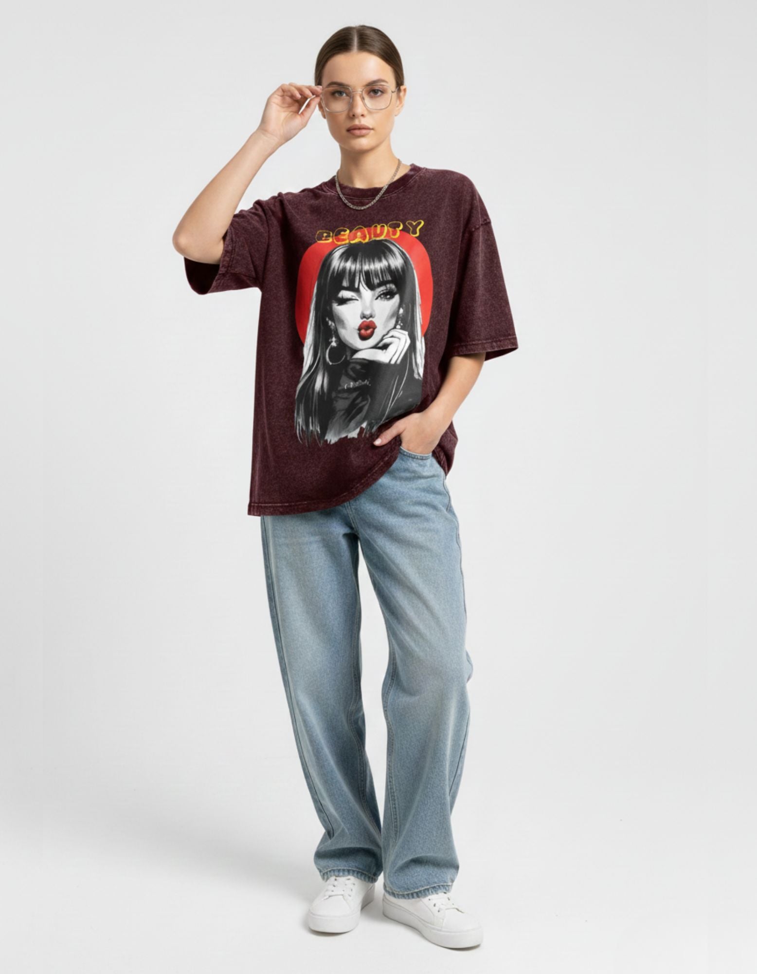 Fashion model posing in a charcoal oversized graphic t-shirt with retro 'Beauty' design and round glasses.