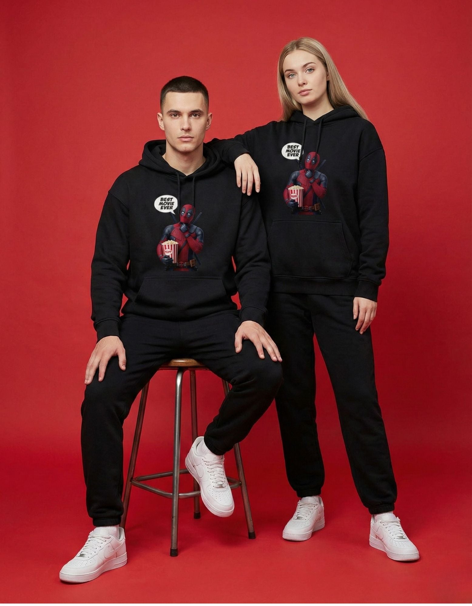 A man and woman wearing matching black Deadpool graphic hoodies on a red background, showcasing GENZs Fashion streetwear.
