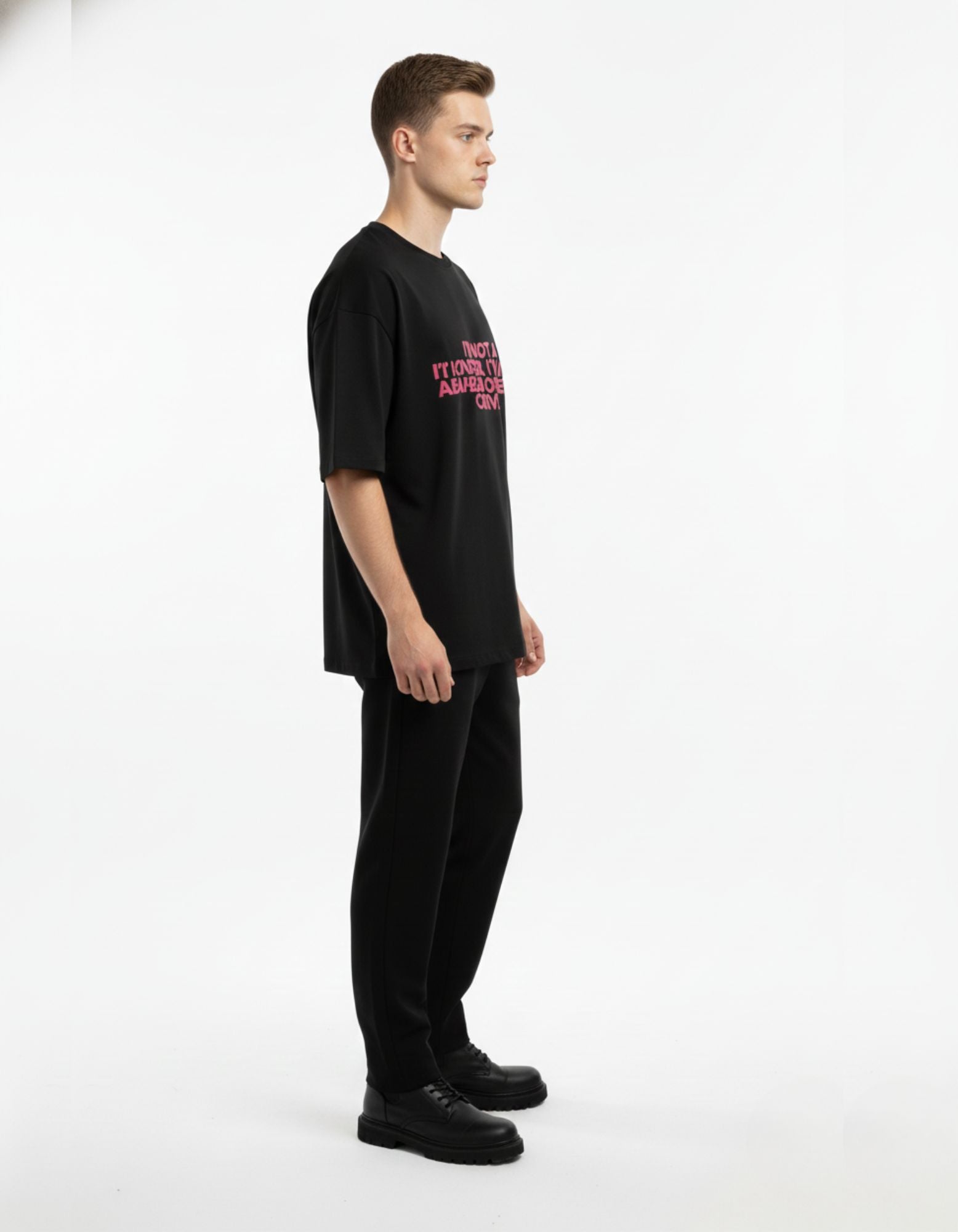 Male model in black oversized drop shoulder t-shirt with pink slogan, perfect for 2025 Indian streetwear trends.