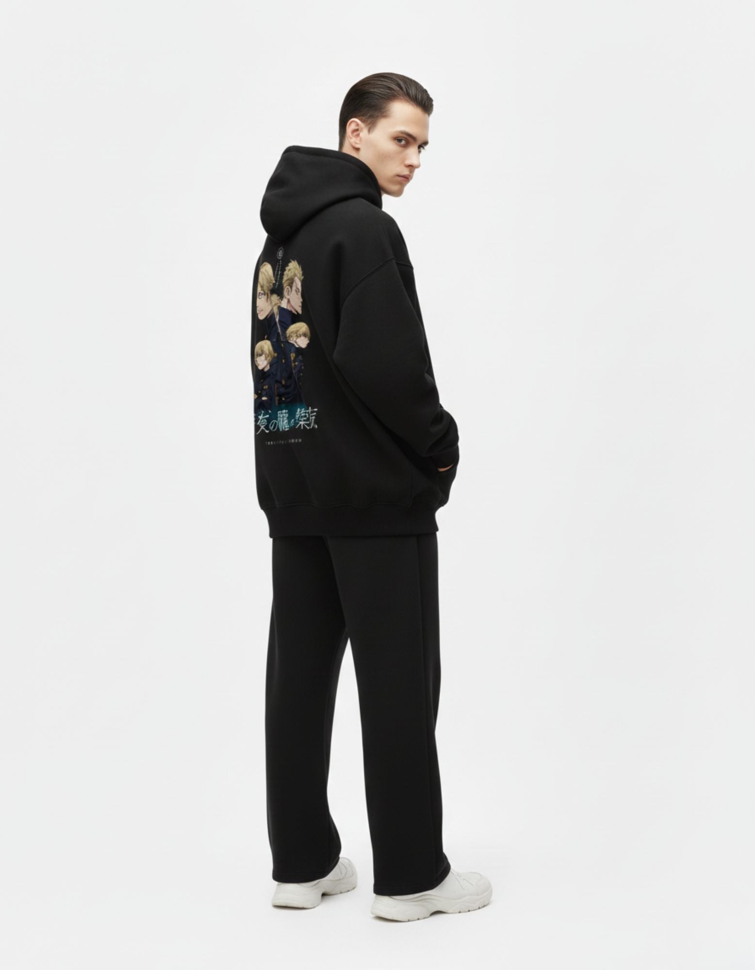 Male model showing the back of a black streetwear hoodie with a high-quality anime character graphic print.