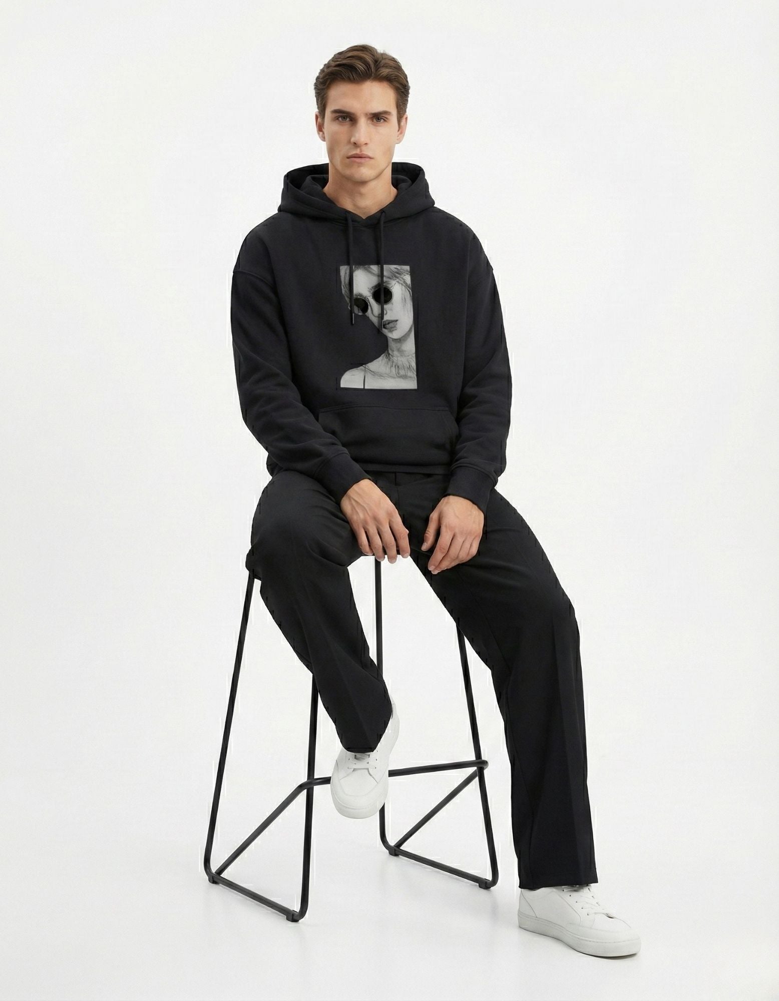 Male model sitting on a stool wearing a black heavy-weight graphic hoodie by GENZs Fashion.