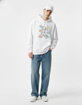 Male model wearing a white "Take it Easy" hoodie with cloud and sun graphics, styled with wide-leg blue jeans.