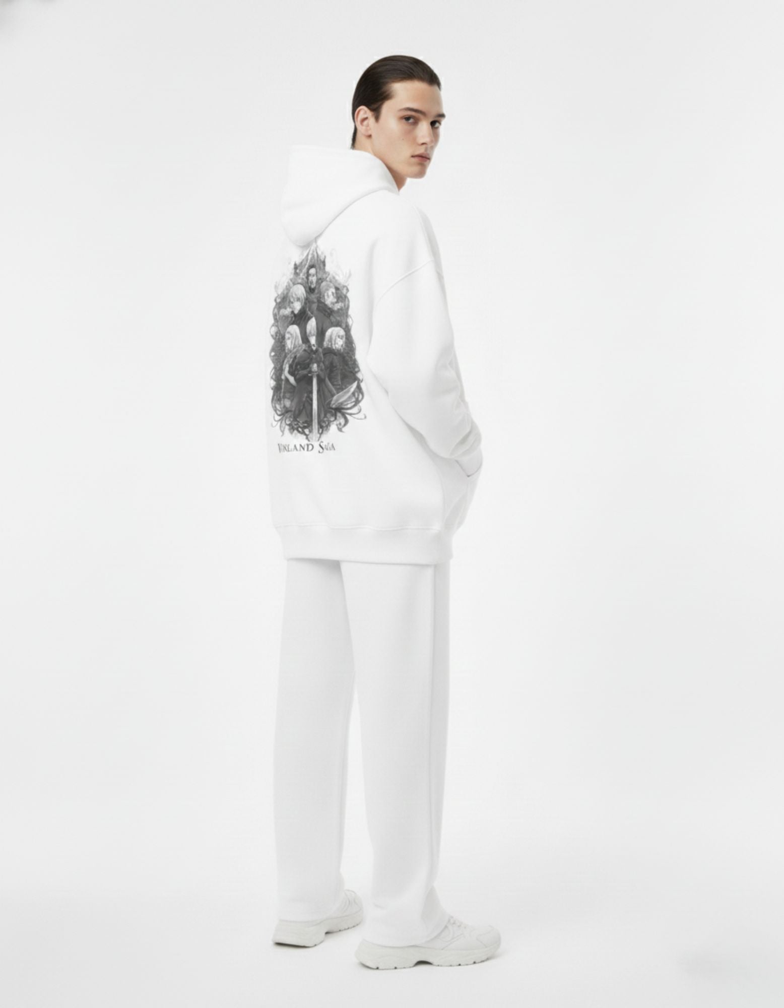 Side view of a male model in a white Vinland Saga graphic hoodie, styled with white streetwear trousers for a clean aesthetic.