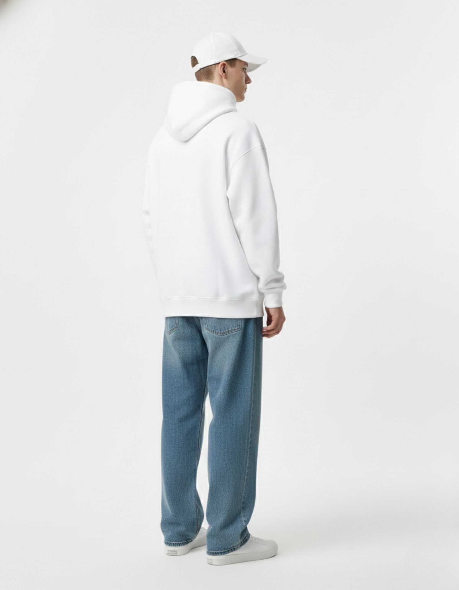 Back view of a male model in a white graphic hoodie and blue jeans, showing the oversized streetwear silhouette.