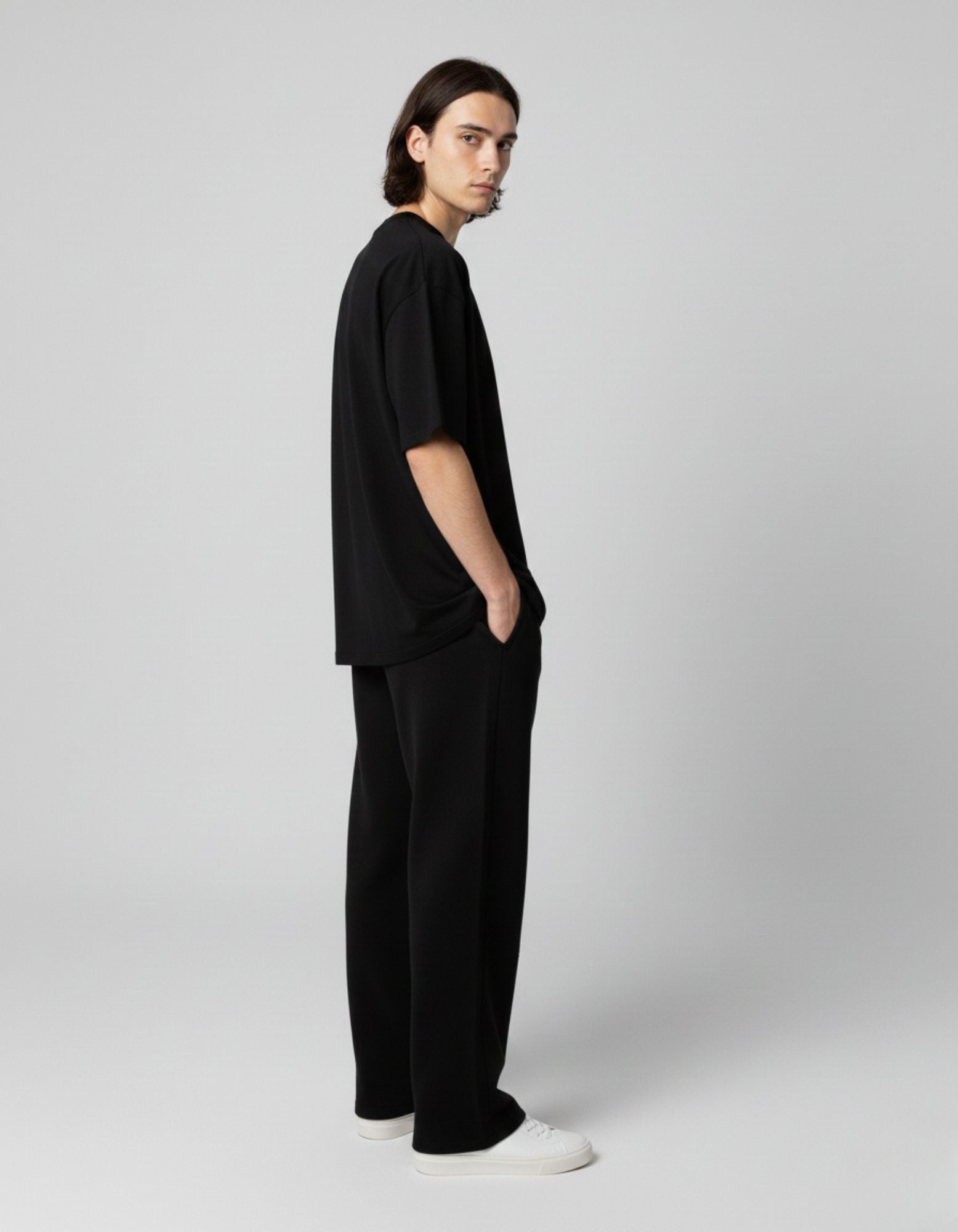 Full side profile of a man in all-black streetwear outfit including an oversized graphic t-shirt and wide-leg trousers.