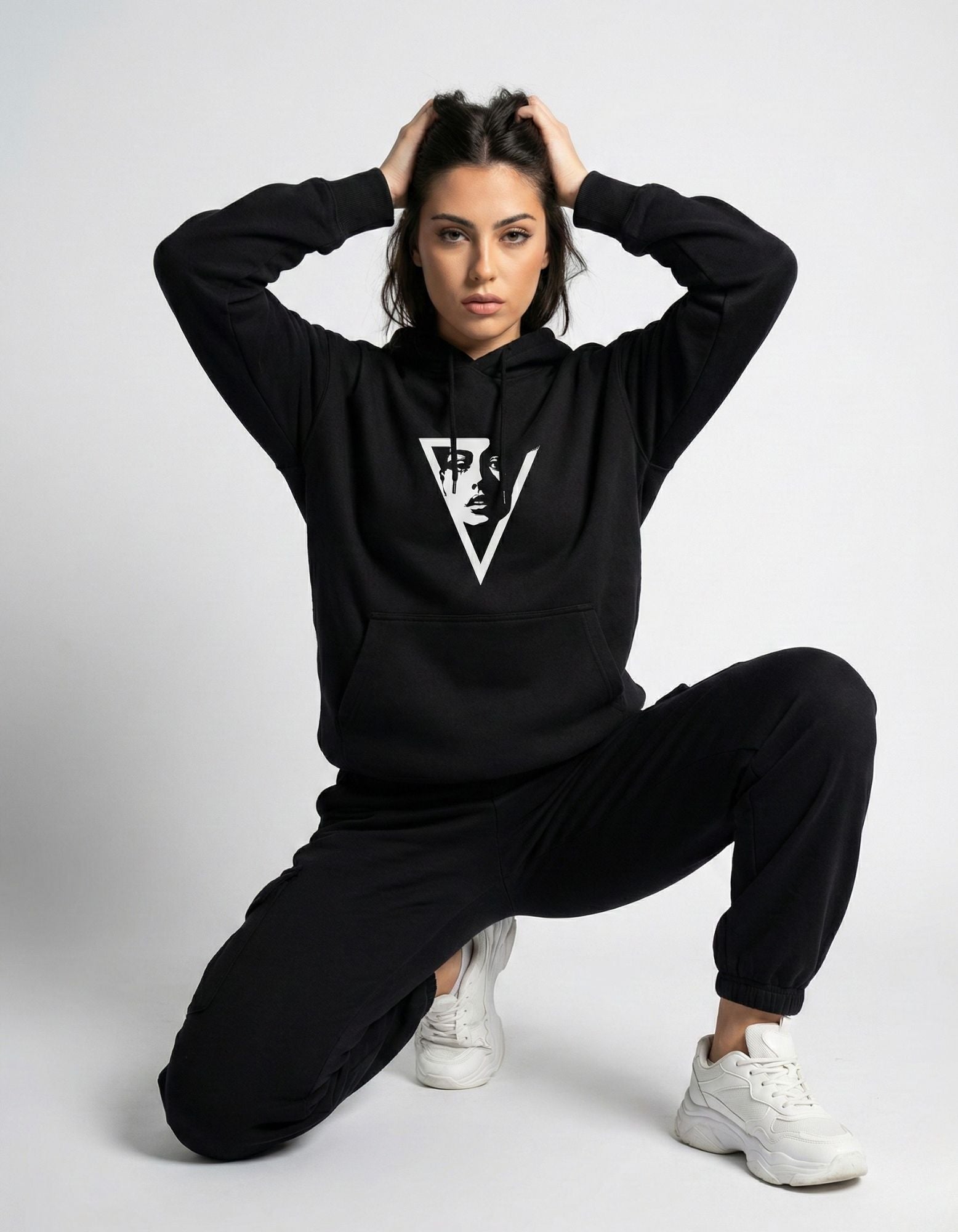 Female model kneeling in an oversized black hoodie with a minimalist aesthetic graphic, ideal for Gen Z streetwear style.