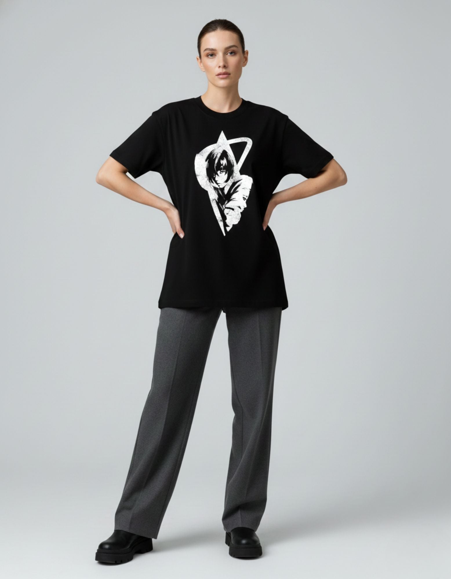 A woman modeling a black oversized graphic t-shirt with anime art, styled with grey trousers for a streetwear look.