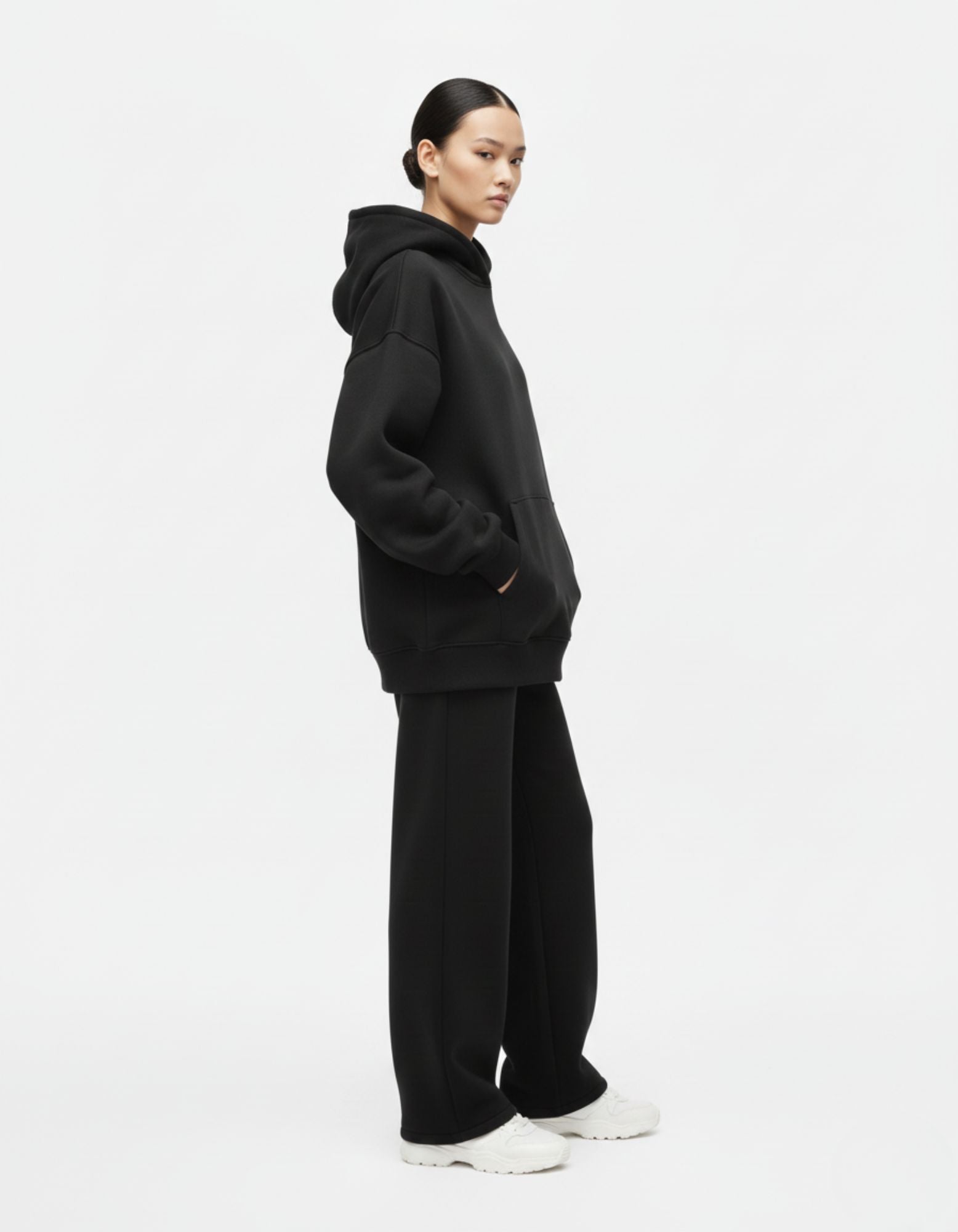 "Side view of a female model wearing a baggy black streetwear hoodie with a hood and large kangaroo pocket from GENZs Fashion."