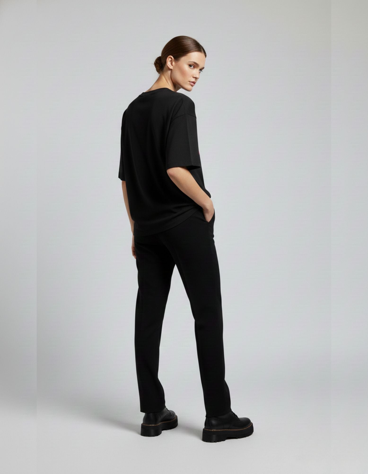 Back view of woman wearing oversized black t-shirt and black pants, showcasing relaxed fit and streetwear silhouette.