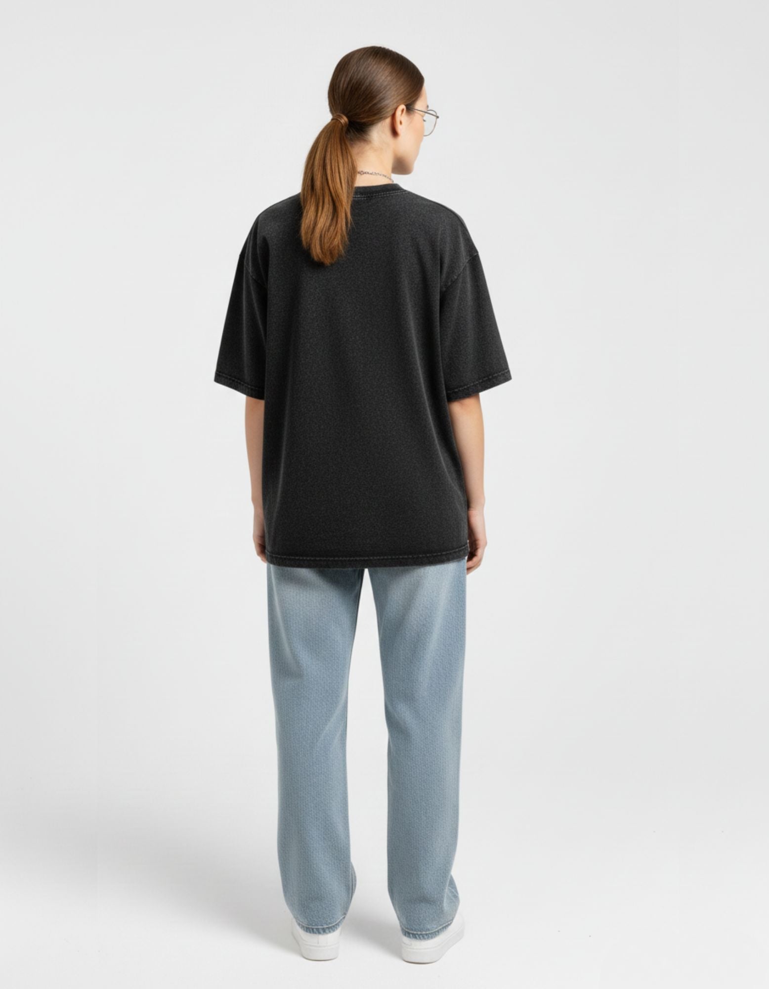 Back view of a loose-fit charcoal streetwear t-shirt on a female model highlighting the drop-shoulder design.