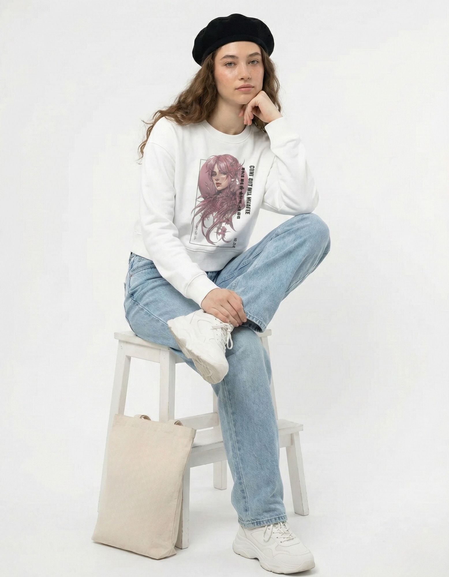 Female model sitting on a stool wearing an oversized white manga-art sweatshirt, representing a relaxed aesthetic streetwear style.