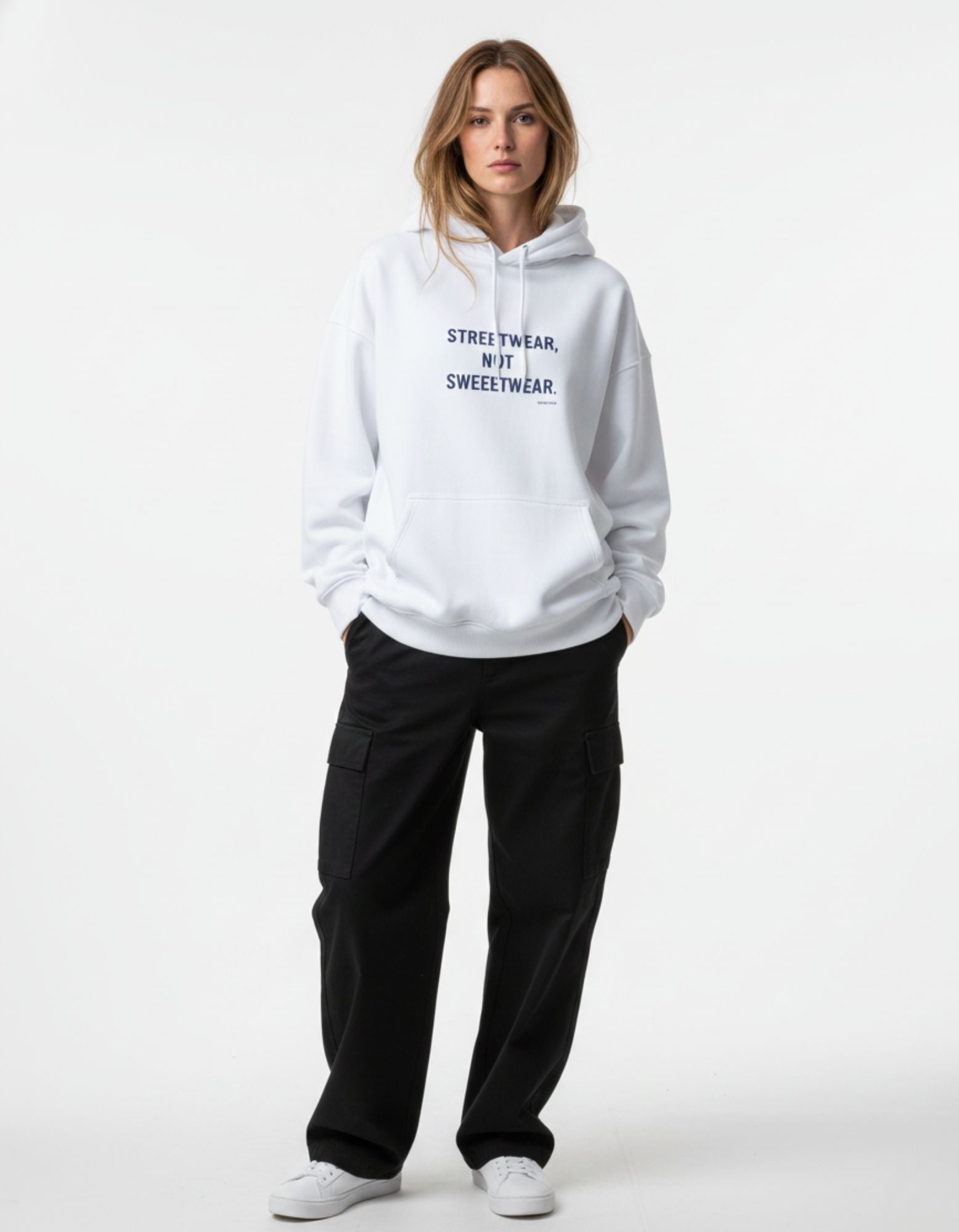 Front view of a female model wearing an oversized white hoodie with a black graphic slogan, styled with black streetwear pants.