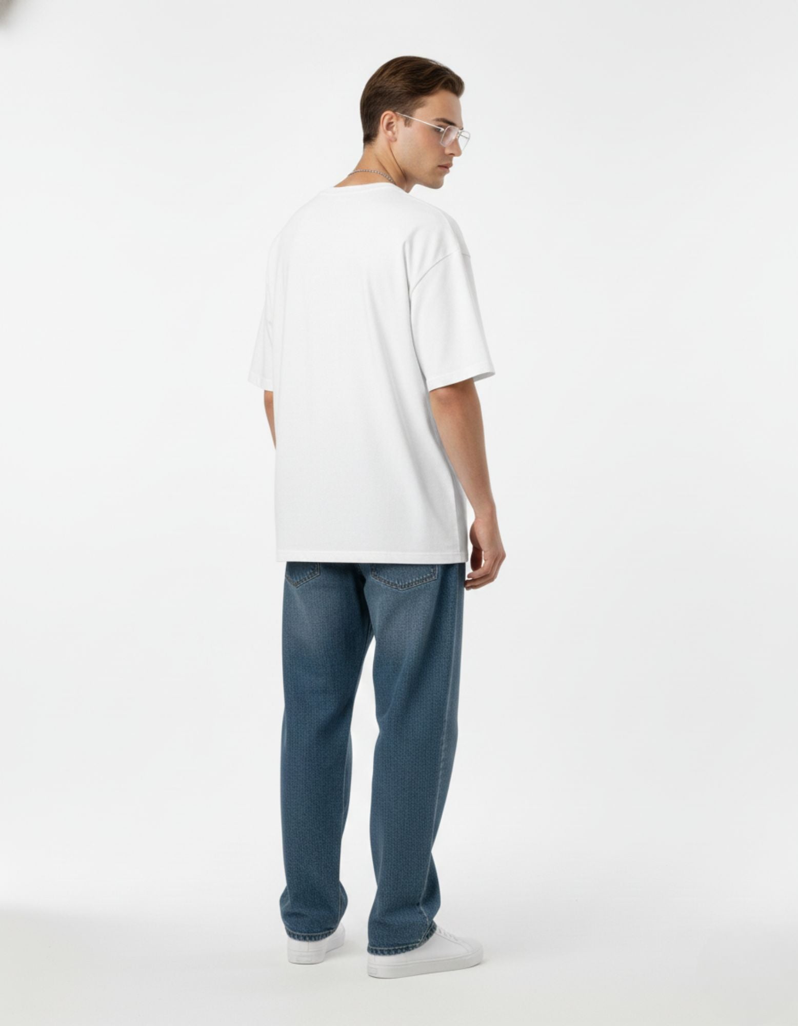 Man wearing plain back white oversized t-shirt with blue jeans, showcasing relaxed streetwear silhouette for 2025 fashion.