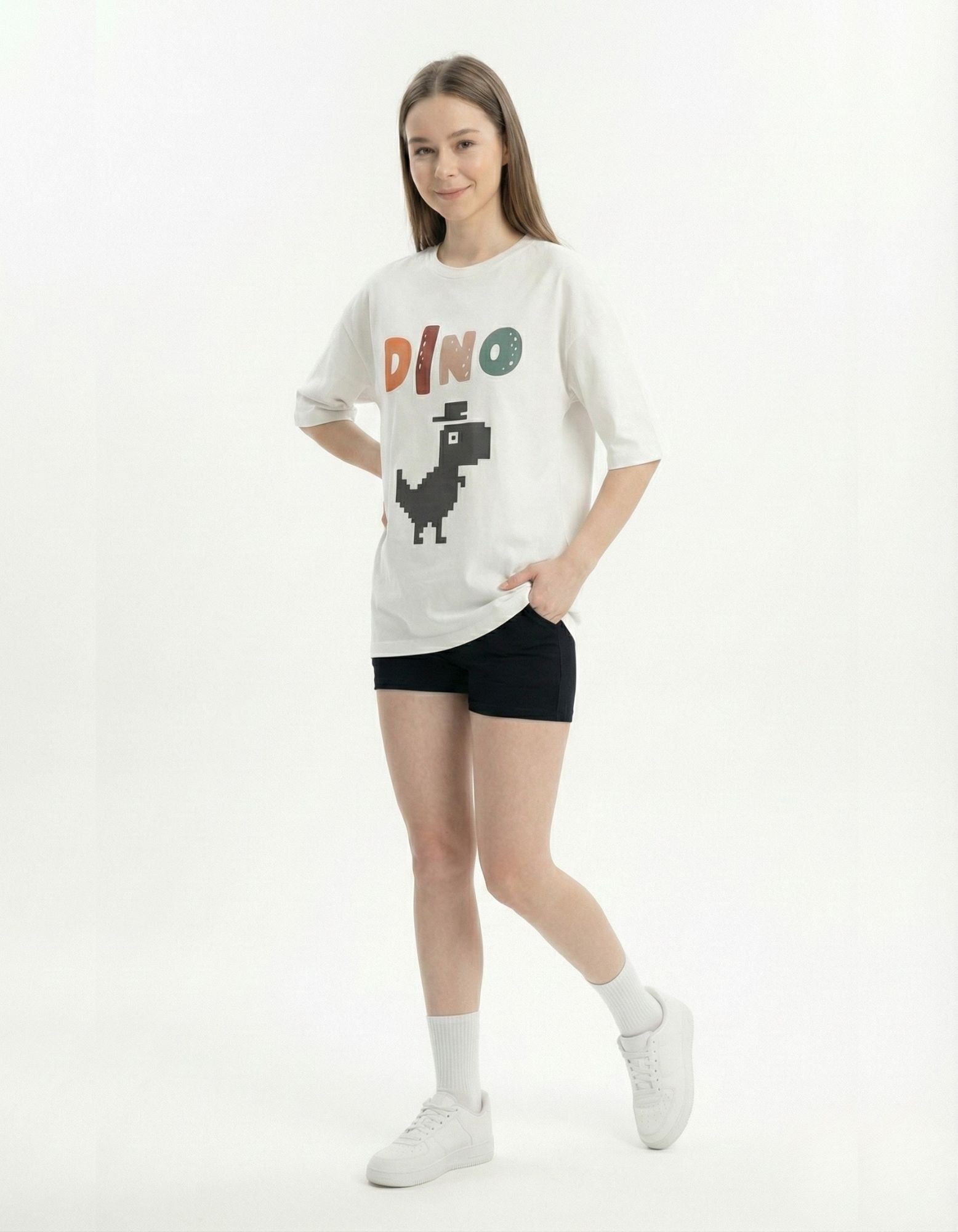 Woman posing in white pixel dino printed tee with black shorts, showcasing a retro gaming vibe for India 2025.