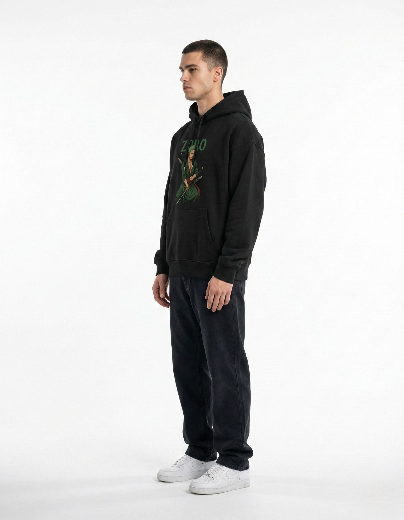 Side profile of a male model wearing a black Roronoa Zoro anime graphic hoodie with dark jeans for a clean streetwear look.