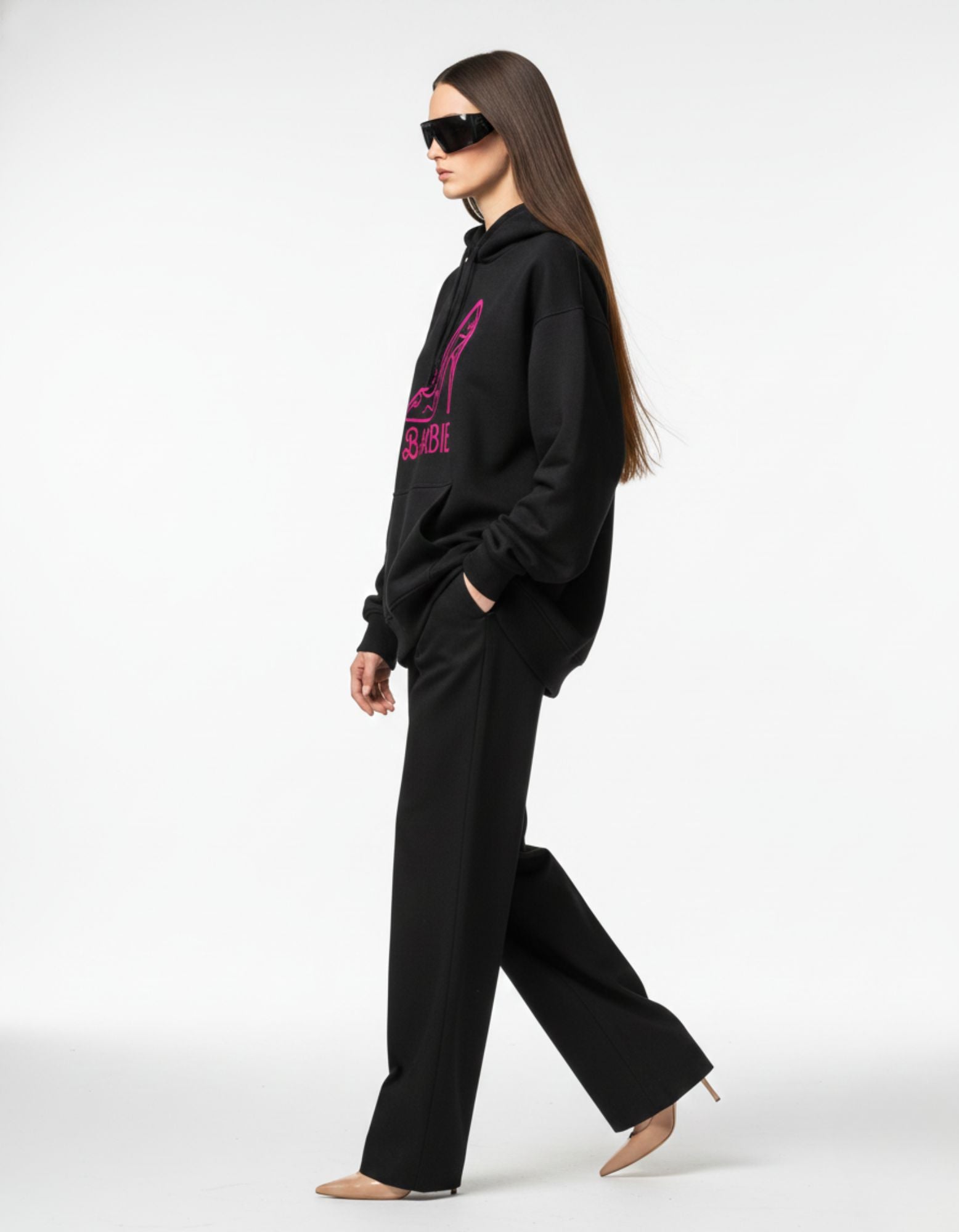 Side view of a model wearing a black Barbie graphic hoodie and sunglasses, showcasing a casual Gen Z streetwear aesthetic.