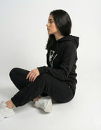 Side profile of a woman sitting and wearing a black streetwear hoodie with a minimalist art print from GENZs Fashion.