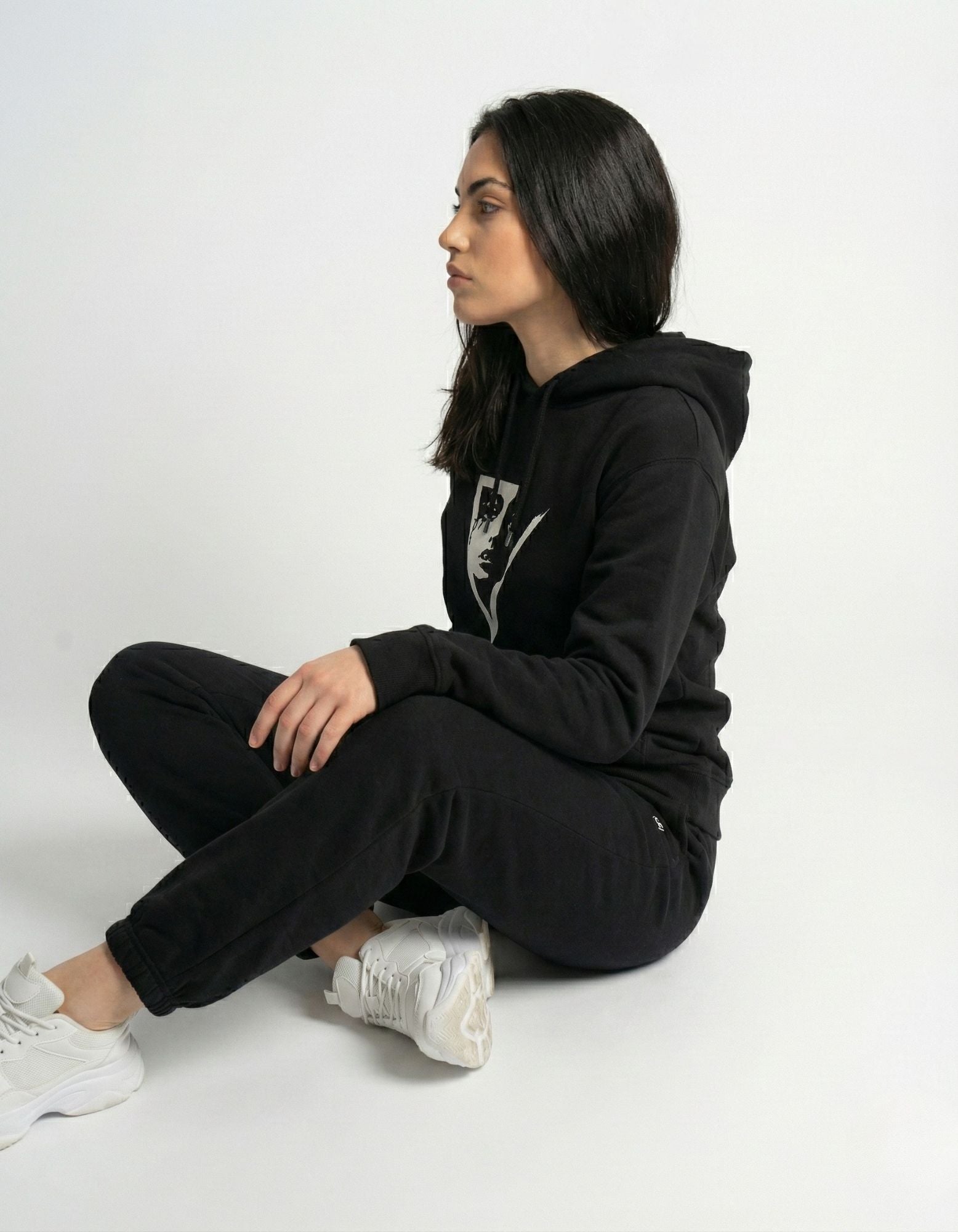 Side profile of a woman sitting and wearing a black streetwear hoodie with a minimalist art print from GENZs Fashion.