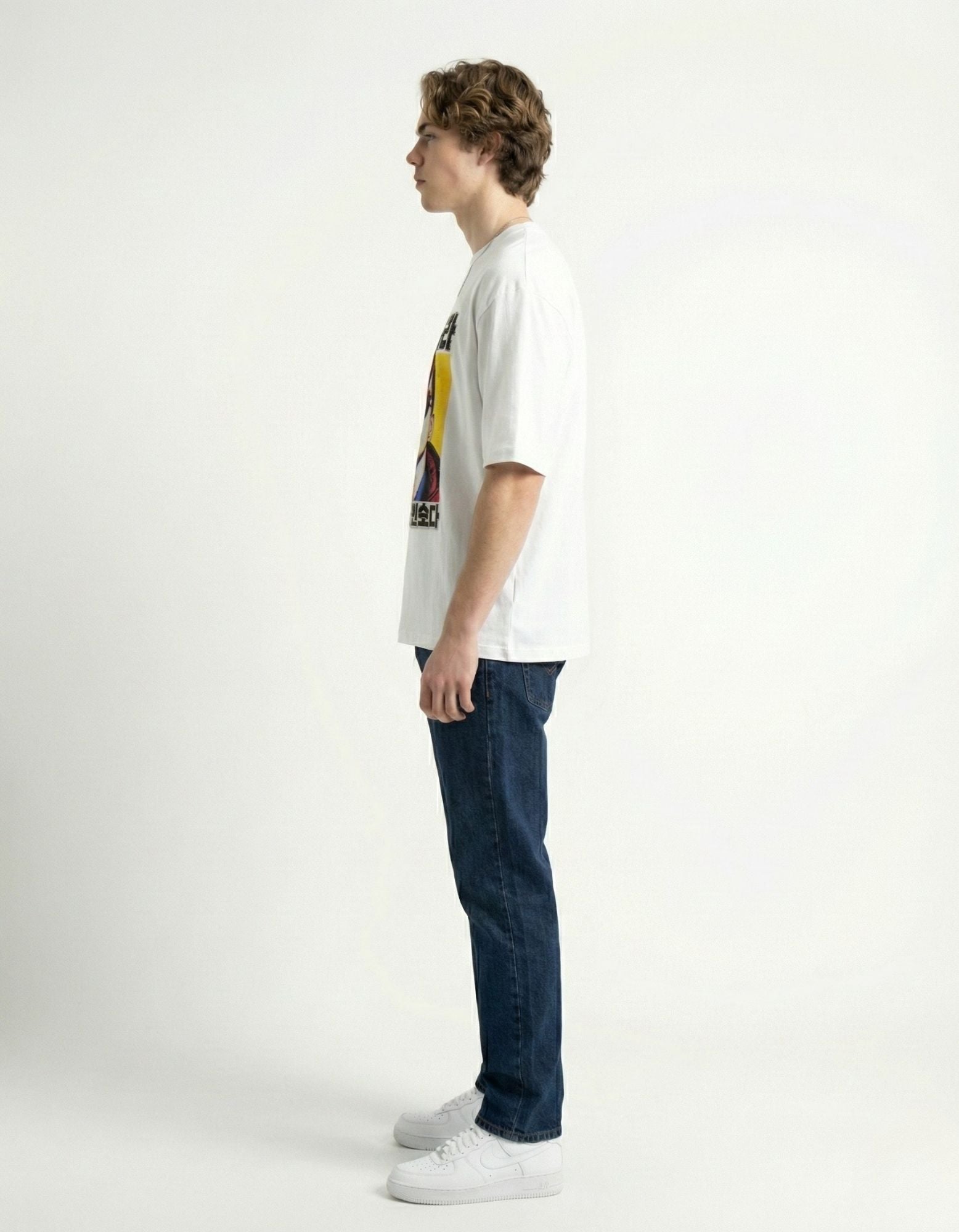 "Side profile of male model wearing a white oversized tee, showing the relaxed drop shoulder fit."