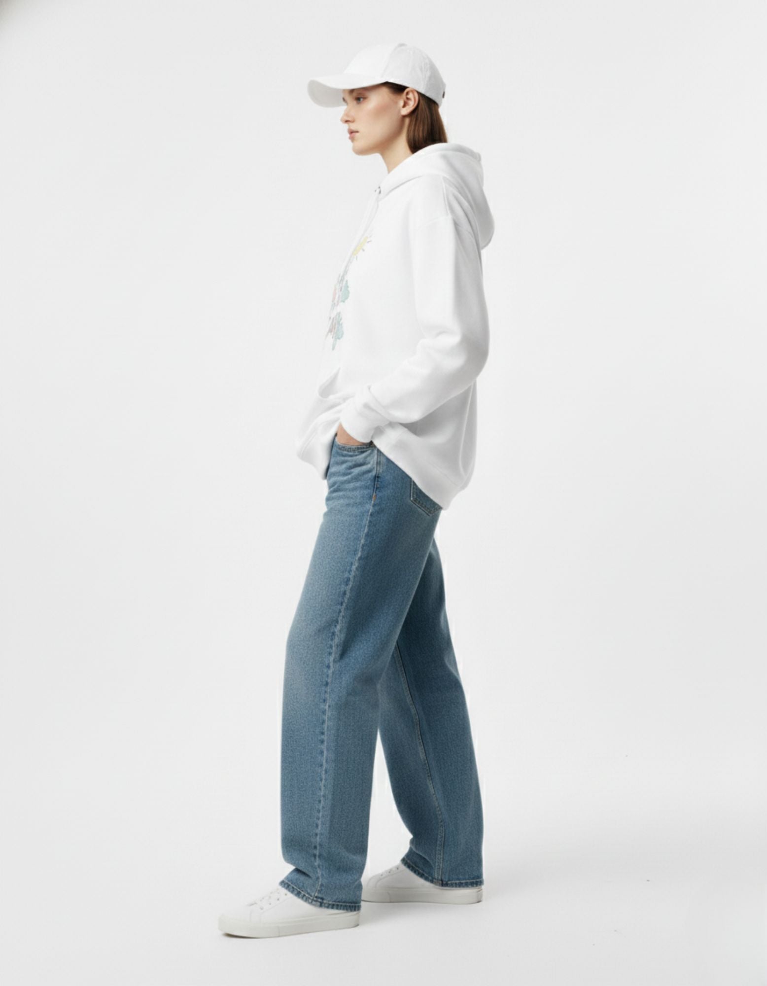 Side view of a female model wearing a white "Take it Easy" graphic hoodie and baggy denim jeans.