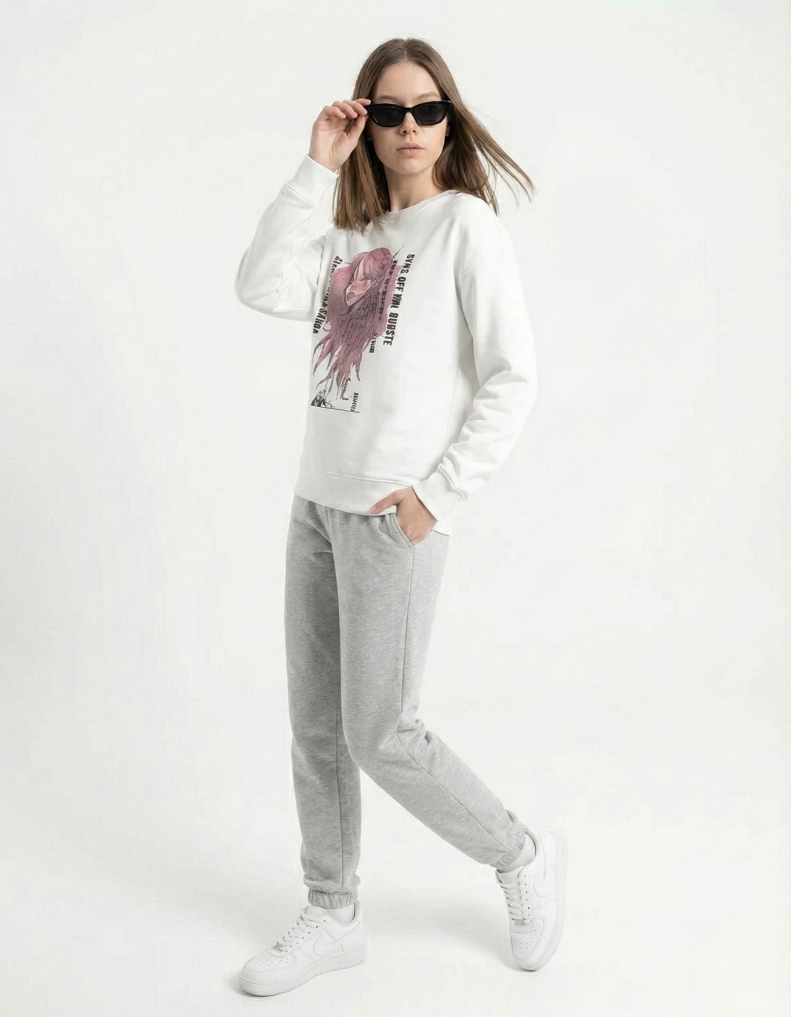 Female model posing in a white anime girl graphic sweatshirt and grey joggers, showcasing a 2025 soft-girl streetwear outfit.