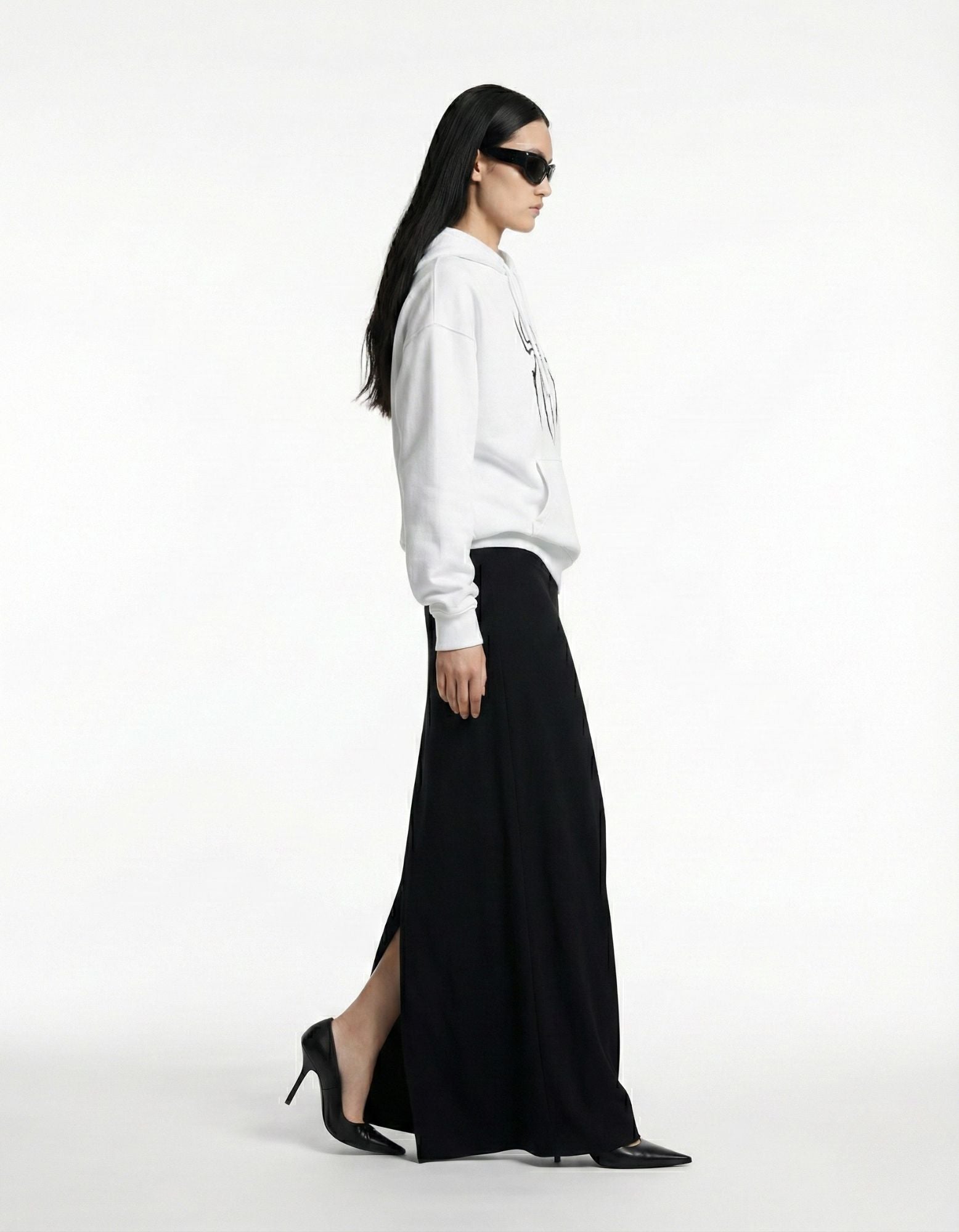 Side view of a female model in a white graphic hoodie with sunglasses, showcasing a modern luxury streetwear look.