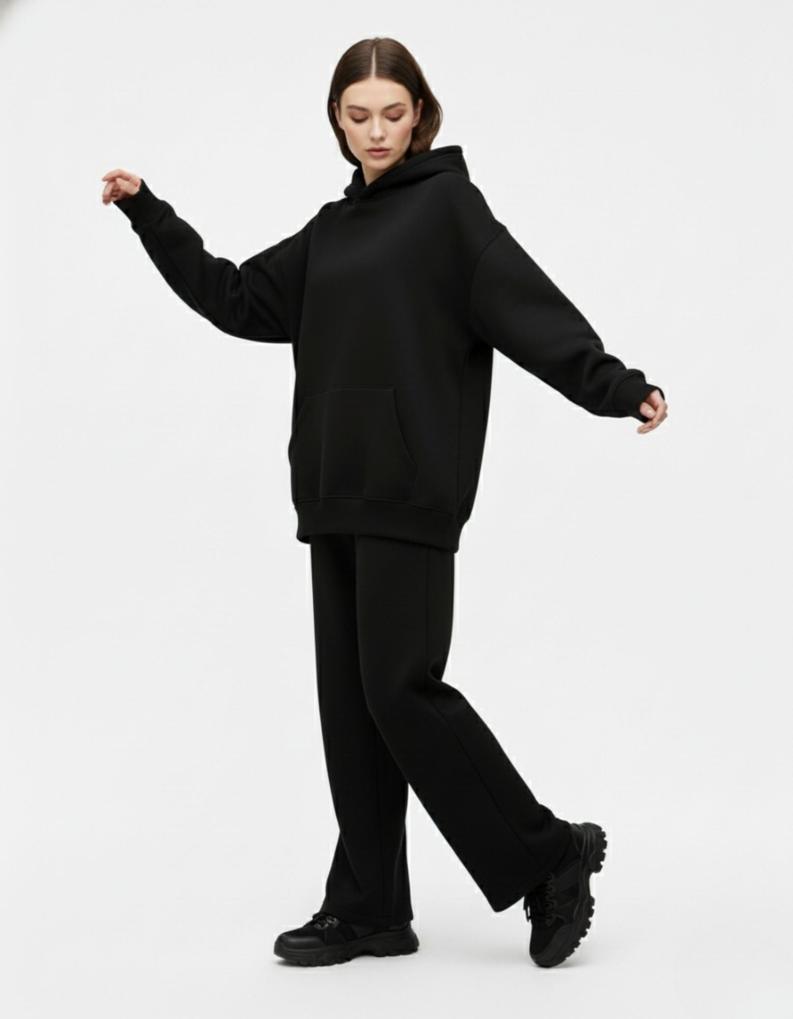 Full standing pose of a model in a black hoodie and matching wide-leg trousers, representing a clean girl streetwear aesthetic.