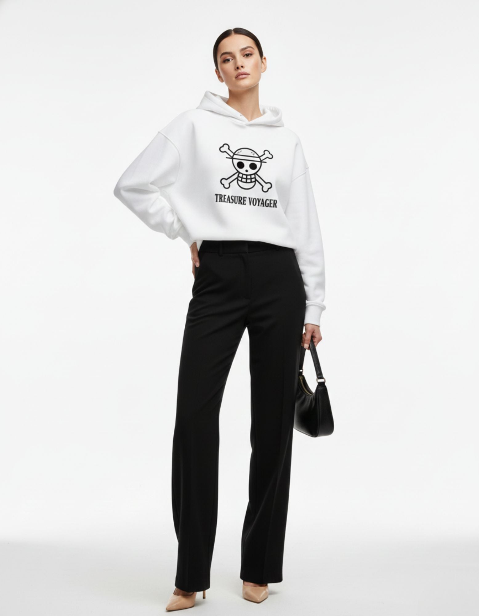 A woman modeling a white Treasure Voyager oversized hoodie with a minimalist skull and crossbones graphic, styled with black trousers.