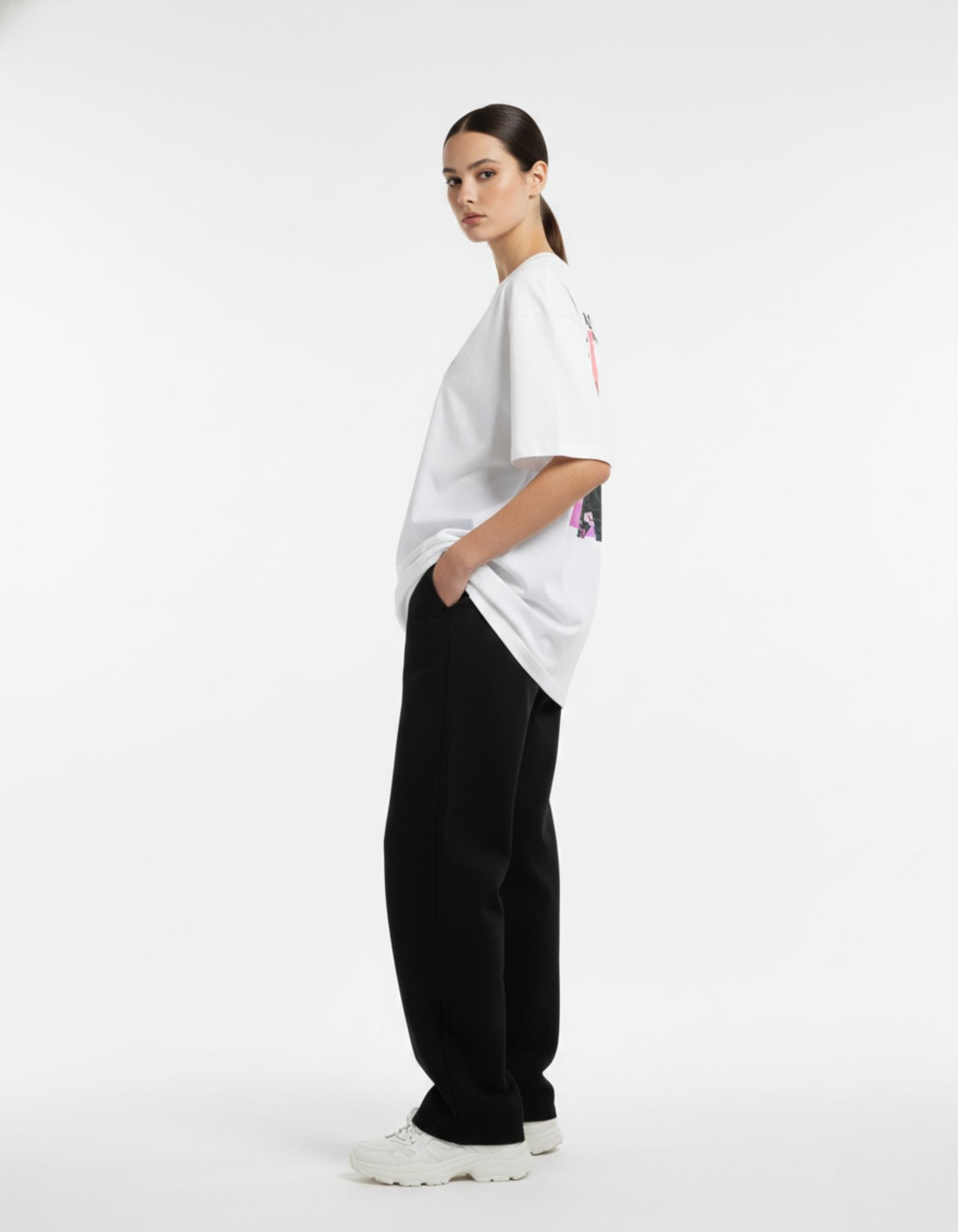 Side profile of a unisex white oversized t-shirt paired with black baggy trousers for a Gen Z streetwear look.