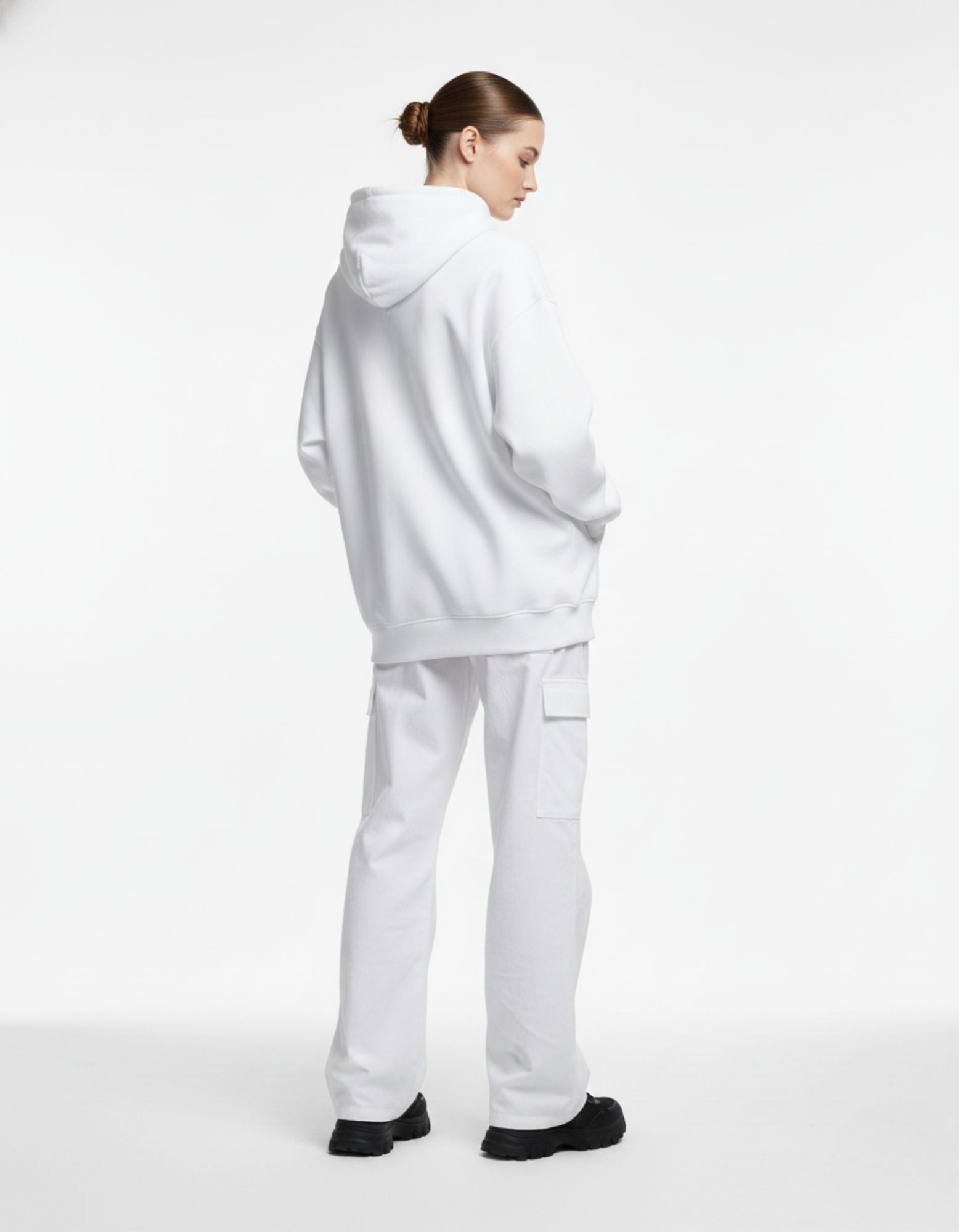 Back view of a woman in a white oversized hoodie and white cargo trousers, highlighting a clean, modern Gen Z fashion silhouette.