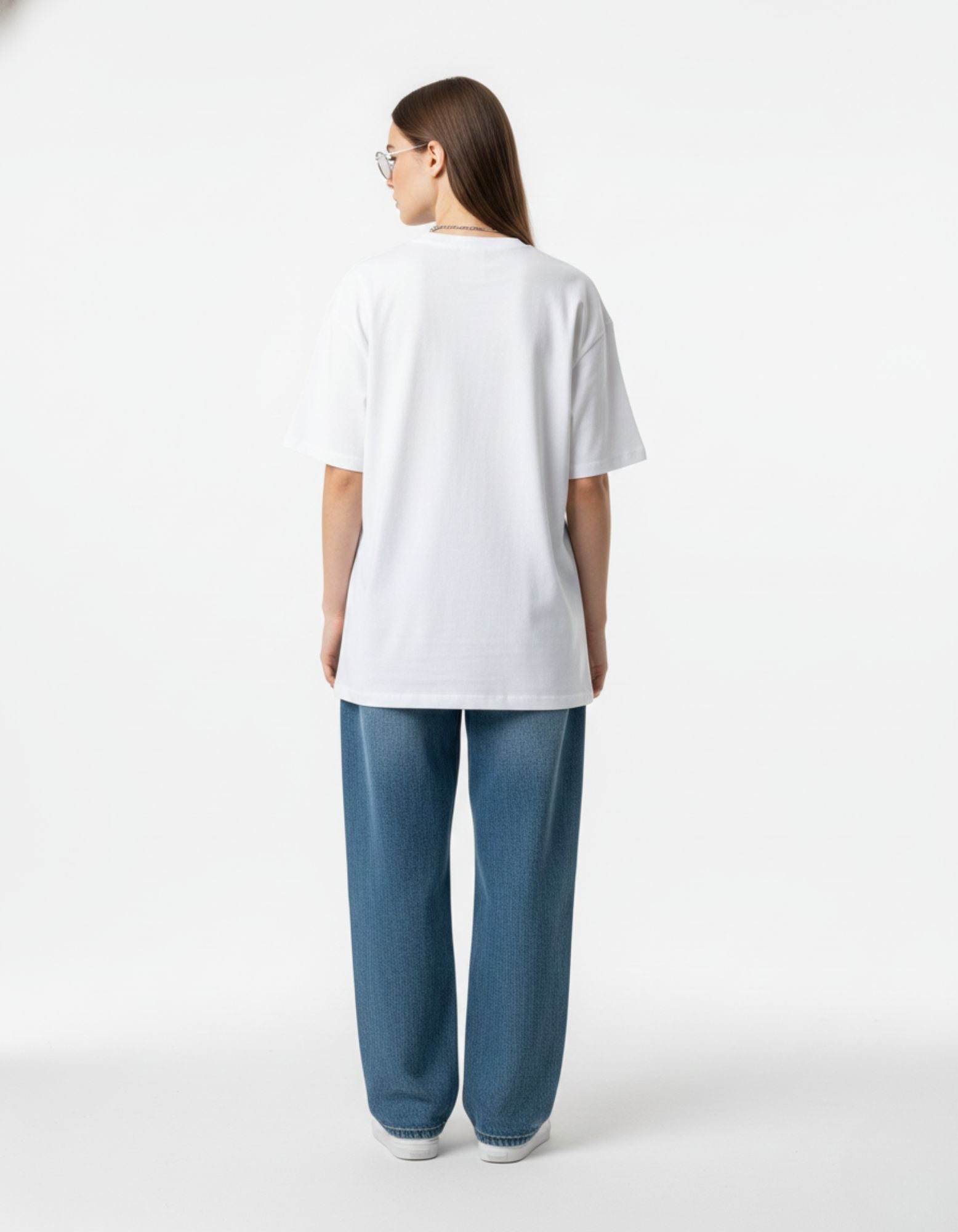 Back view of woman wearing white oversized t-shirt and blue jeans, relaxed streetwear fit for urban Indian style.