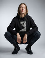 Female model squatting in a GENZs Fashion black hoodie featuring a grayscale portrait graphic print.